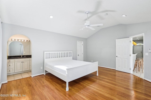 unfurnished bedroom featuring light wood finished floors, ensuite bathroom, lofted ceiling, and a sink