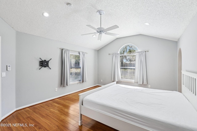 bedroom with multiple windows, arched walkways, wood finished floors, and vaulted ceiling