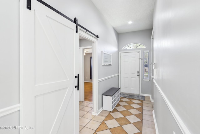 doorway to outside with a barn door, light tile patterned floors, baseboards, and a textured ceiling