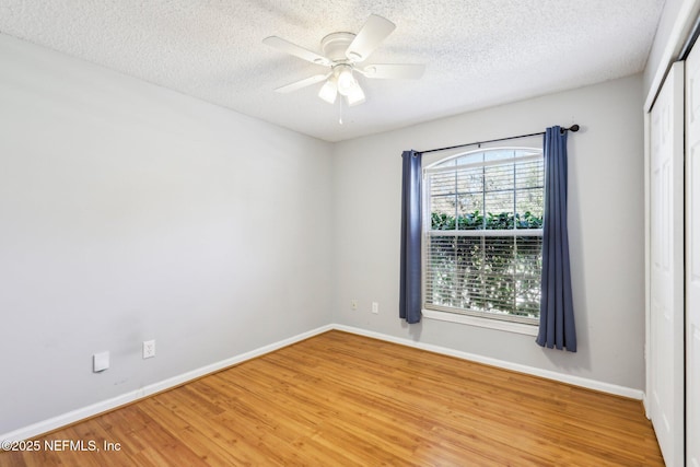 empty room with a ceiling fan, light wood-style floors, baseboards, and a textured ceiling