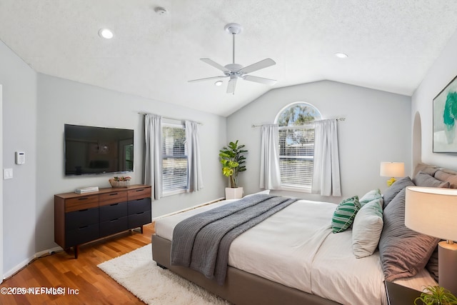 bedroom with baseboards, light wood-style flooring, ceiling fan, vaulted ceiling, and a textured ceiling