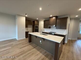 kitchen with stainless steel microwave, oven, dark brown cabinetry, light countertops, and a sink