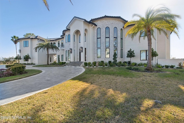 mediterranean / spanish-style home featuring curved driveway, a tile roof, a front yard, and stucco siding