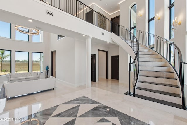 staircase featuring visible vents, marble finish floor, an inviting chandelier, baseboards, and a towering ceiling