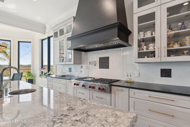 kitchen featuring stainless steel gas cooktop, a sink, custom range hood, crown molding, and tasteful backsplash