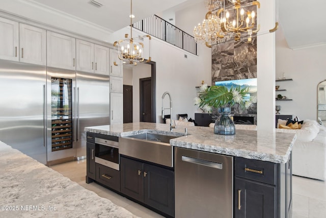 kitchen with a notable chandelier, a sink, light stone counters, appliances with stainless steel finishes, and hanging light fixtures