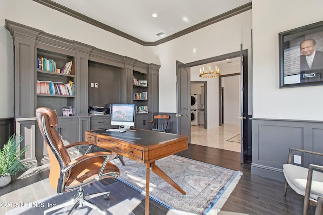 home office with stacked washer and clothes dryer, ornamental molding, wood finished floors, wainscoting, and a chandelier