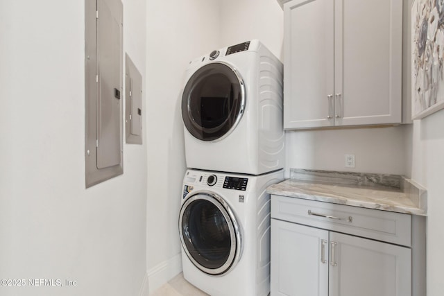 clothes washing area featuring electric panel, cabinet space, stacked washer / drying machine, and baseboards