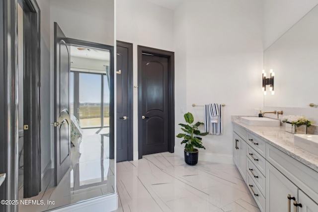 bathroom with a sink, baseboards, marble finish floor, and double vanity