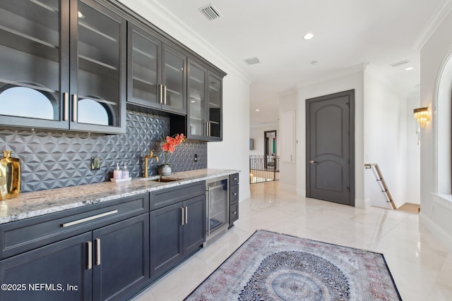 kitchen featuring light stone countertops, visible vents, ornamental molding, a sink, and wine cooler