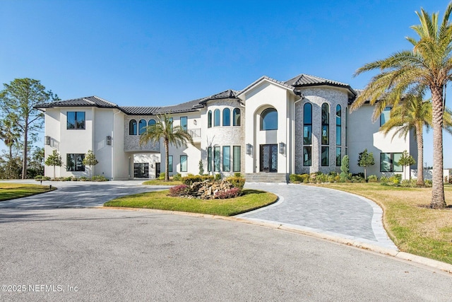 view of front of house with stucco siding, curved driveway, a front yard, and a tile roof