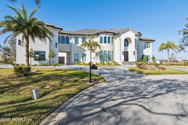 view of front of house with a front yard, stucco siding, a tile roof, and curved driveway