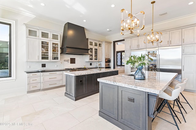 kitchen with a center island with sink, an inviting chandelier, custom range hood, crown molding, and tasteful backsplash