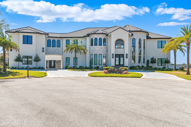 mediterranean / spanish house featuring stucco siding, french doors, a tile roof, and curved driveway