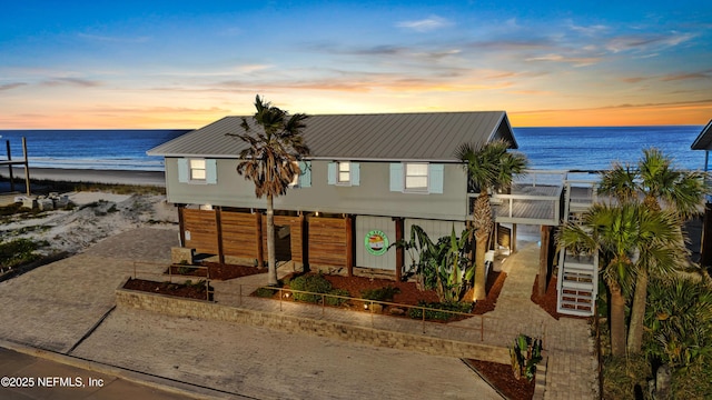 view of front of home with a view of the beach, a water view, stairway, metal roof, and driveway