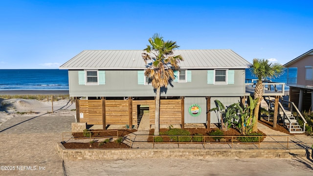 view of front of house with metal roof, a water view, driveway, and a view of the beach