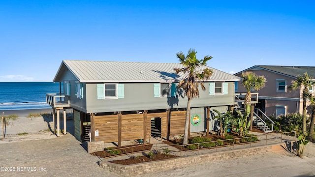 view of front of home featuring a view of the beach, a water view, stairway, metal roof, and decorative driveway