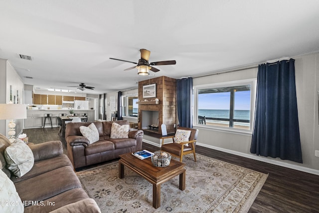 living area featuring wood finished floors, visible vents, baseboards, ceiling fan, and a water view