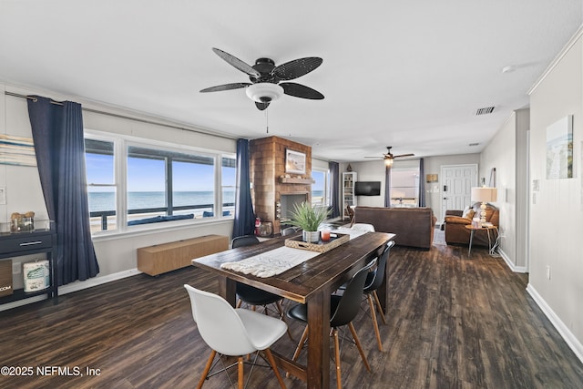 dining space with visible vents, a large fireplace, baseboards, and wood finished floors