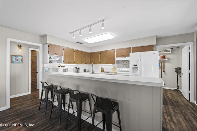 kitchen with dark wood-type flooring, white fridge with ice dispenser, brown cabinetry, light countertops, and stove