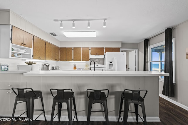 kitchen with visible vents, brown cabinets, dark wood-type flooring, white fridge with ice dispenser, and light countertops