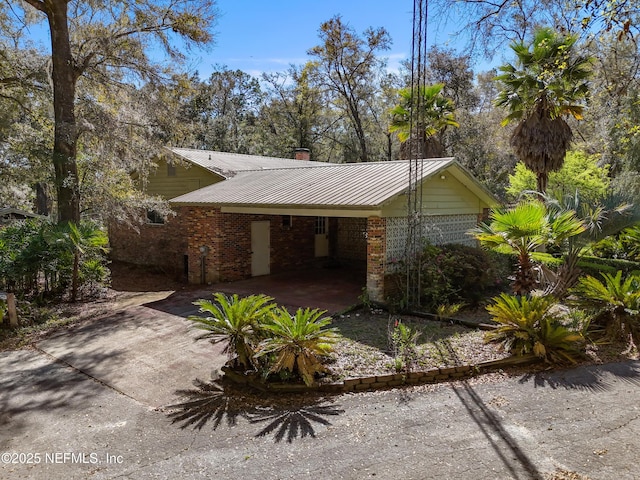 view of property exterior featuring metal roof, an attached carport, brick siding, and driveway