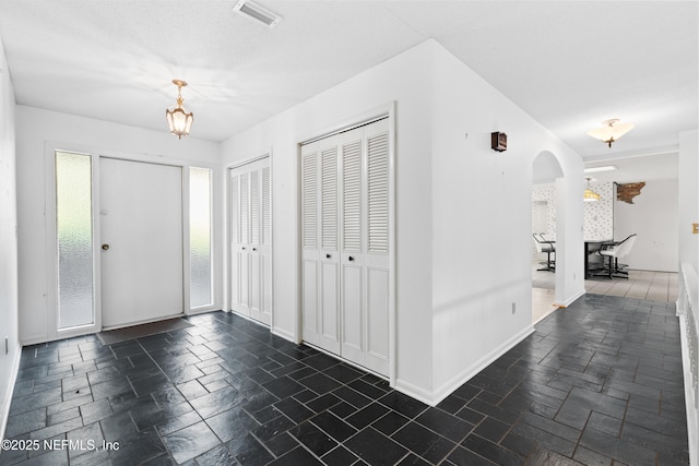 foyer entrance with stone tile floors, visible vents, arched walkways, and baseboards