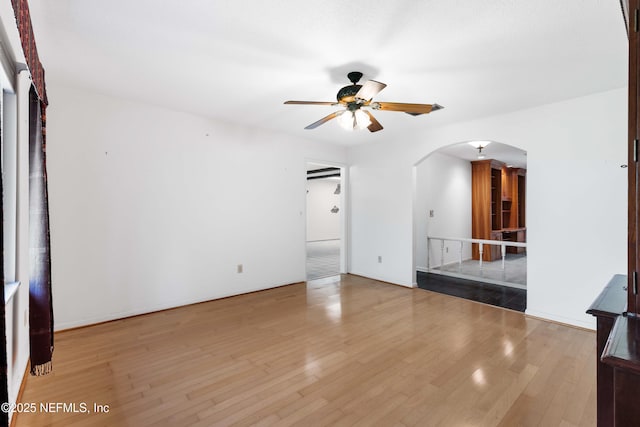 unfurnished living room with arched walkways, wood finished floors, and a ceiling fan