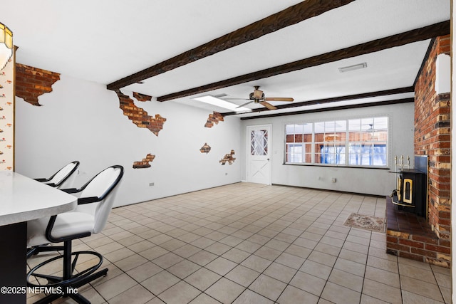 home office with visible vents, beam ceiling, a ceiling fan, light tile patterned floors, and a wood stove