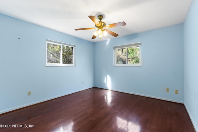 spare room featuring baseboards, a healthy amount of sunlight, dark wood finished floors, and a ceiling fan