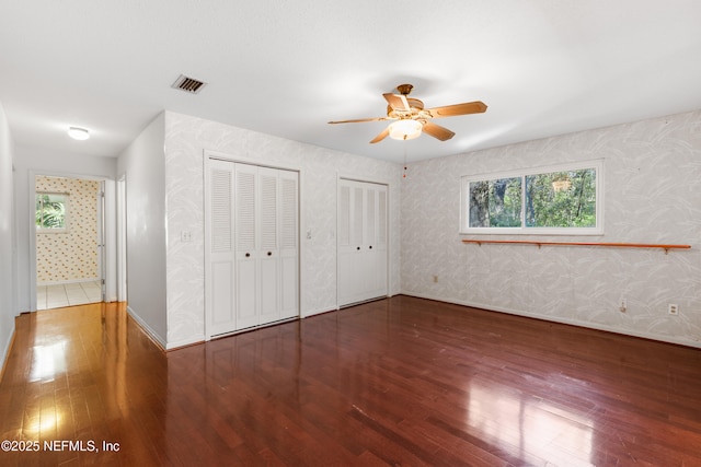 unfurnished bedroom with visible vents, two closets, wallpapered walls, and hardwood / wood-style flooring