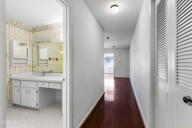 corridor featuring wallpapered walls, baseboards, and a sink