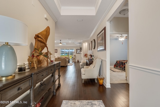 hallway featuring dark wood finished floors, crown molding, and a tray ceiling