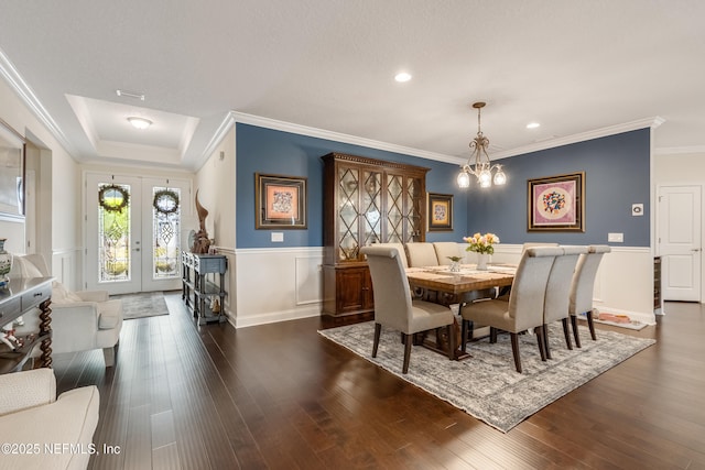 dining room featuring wood finished floors, french doors, wainscoting, crown molding, and a chandelier