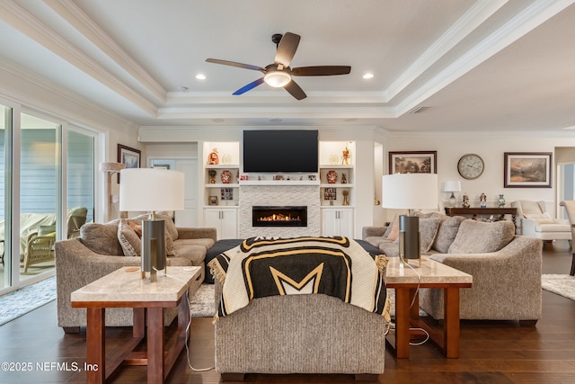 living room featuring a glass covered fireplace, a tray ceiling, visible vents, and dark wood-style floors