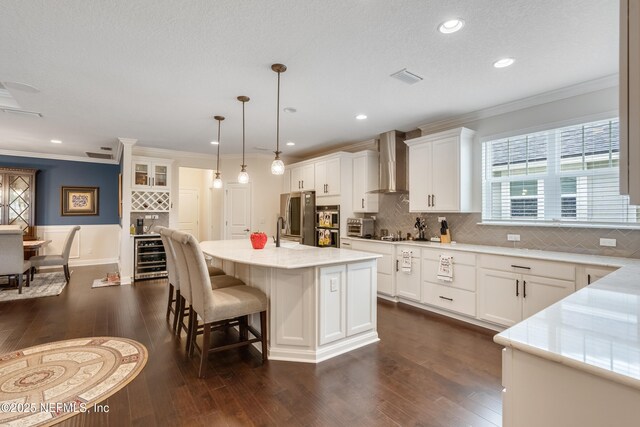 kitchen featuring beverage cooler, dark wood finished floors, white cabinets, crown molding, and wall chimney range hood