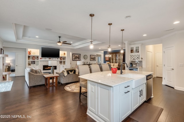 kitchen with dishwasher, a breakfast bar, a glass covered fireplace, white cabinetry, and a sink