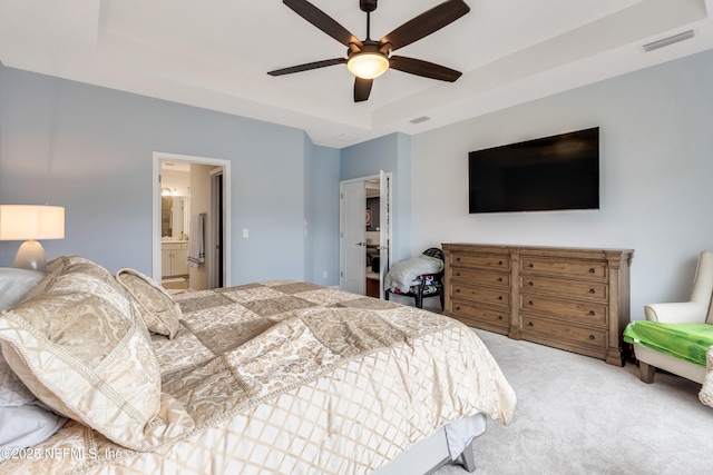 carpeted bedroom with a raised ceiling, visible vents, ensuite bathroom, and ceiling fan