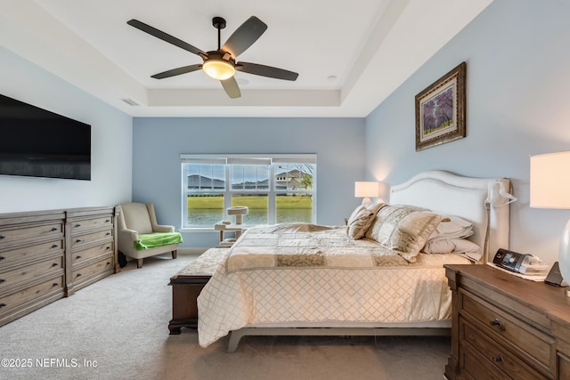 carpeted bedroom with visible vents, a raised ceiling, and a ceiling fan