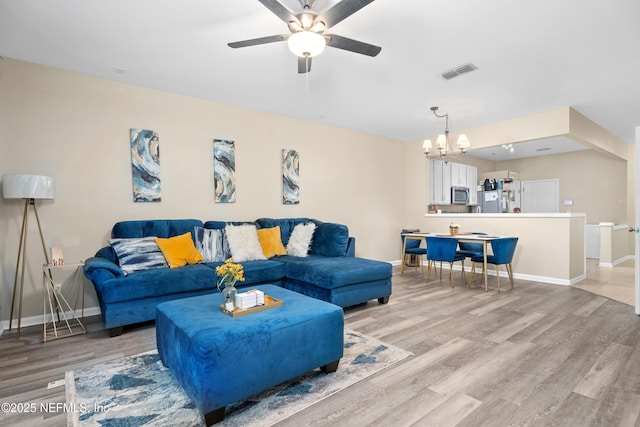 living area featuring visible vents, light wood-style flooring, ceiling fan with notable chandelier, and baseboards