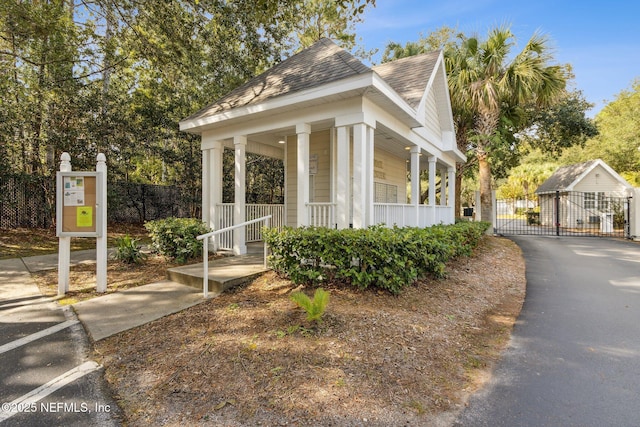 view of property exterior featuring a gate, fence, covered porch, and roof with shingles