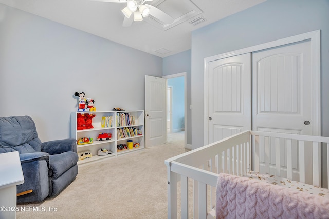 carpeted bedroom featuring visible vents, a nursery area, a closet, and a ceiling fan