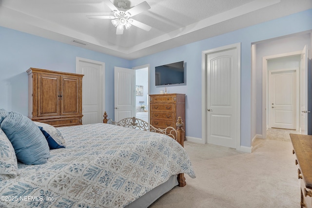 bedroom with baseboards, visible vents, a tray ceiling, ceiling fan, and light carpet