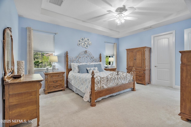 bedroom featuring a tray ceiling, light colored carpet, visible vents, and ceiling fan