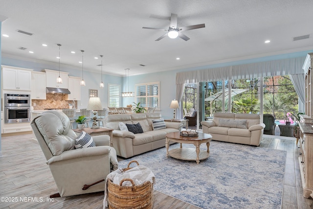 living area featuring visible vents, ceiling fan with notable chandelier, crown molding, and light wood-type flooring