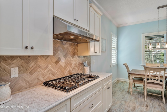 kitchen with stainless steel gas stovetop, white cabinets, under cabinet range hood, crown molding, and tasteful backsplash