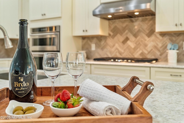 kitchen with decorative backsplash, white cabinetry, under cabinet range hood, and stainless steel appliances