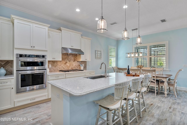 kitchen with light wood finished floors, visible vents, under cabinet range hood, stainless steel appliances, and a sink