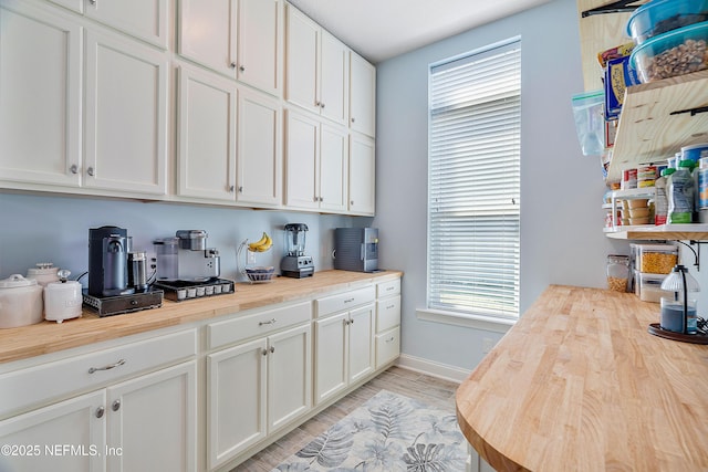 kitchen with light wood finished floors, white cabinets, wood counters, and baseboards