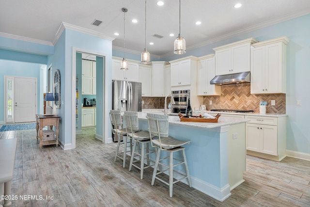 kitchen featuring visible vents, under cabinet range hood, a breakfast bar, light wood-style floors, and a kitchen island with sink